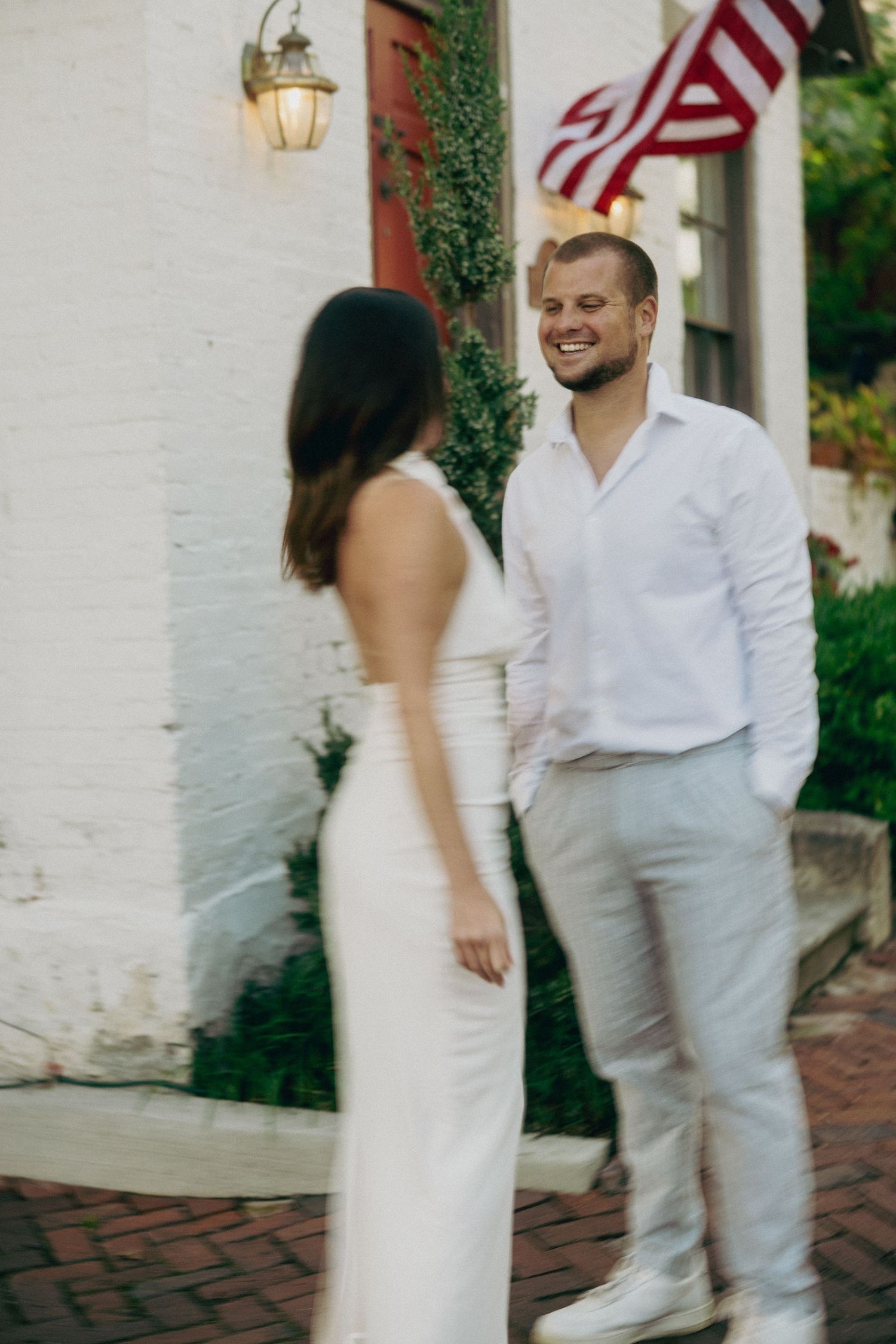 Couple strolling past white colonial buildings on brick sidewalk.