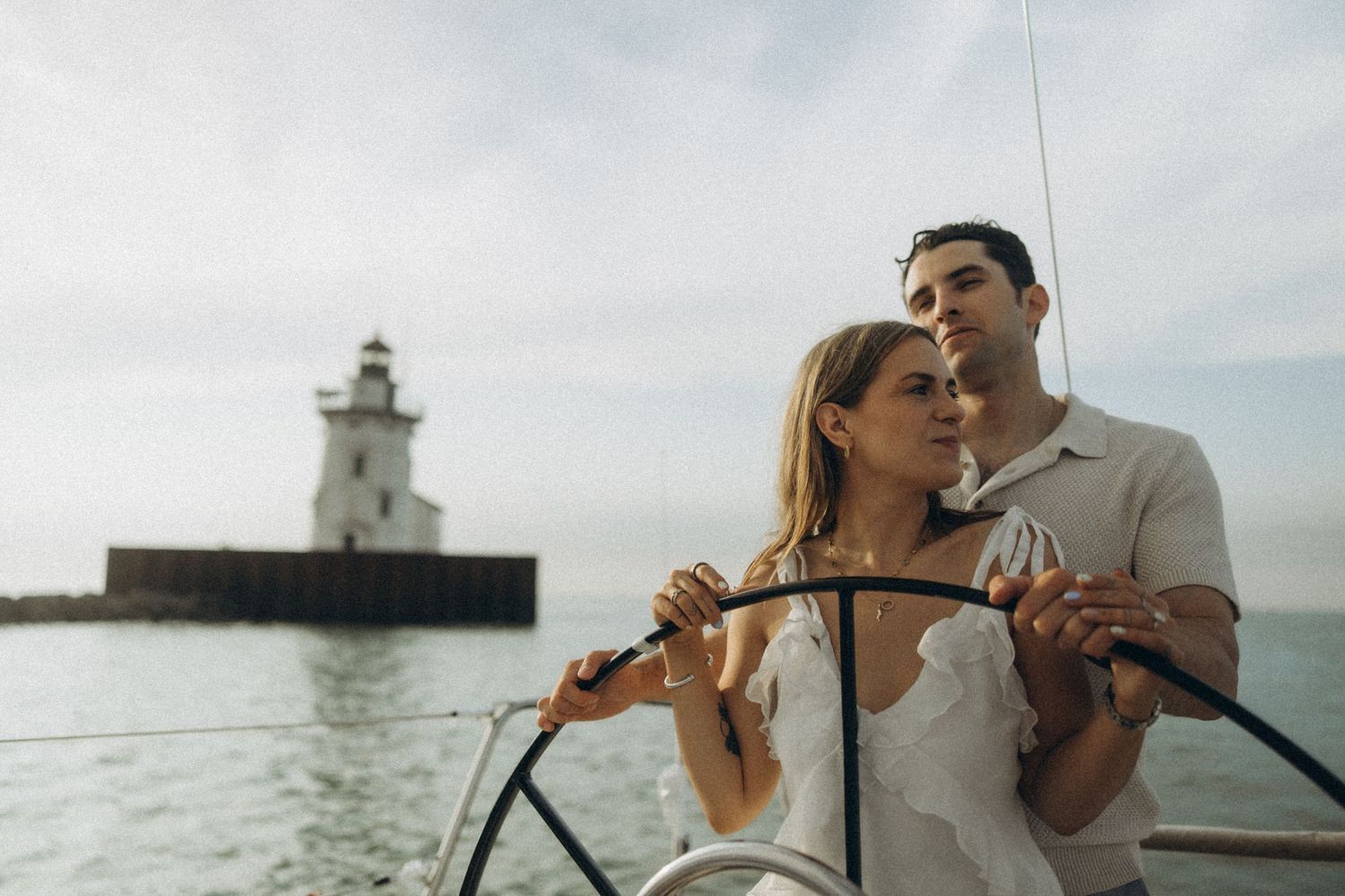 A couple sharing a romantic moment on a boat with a lighthouse in the background.