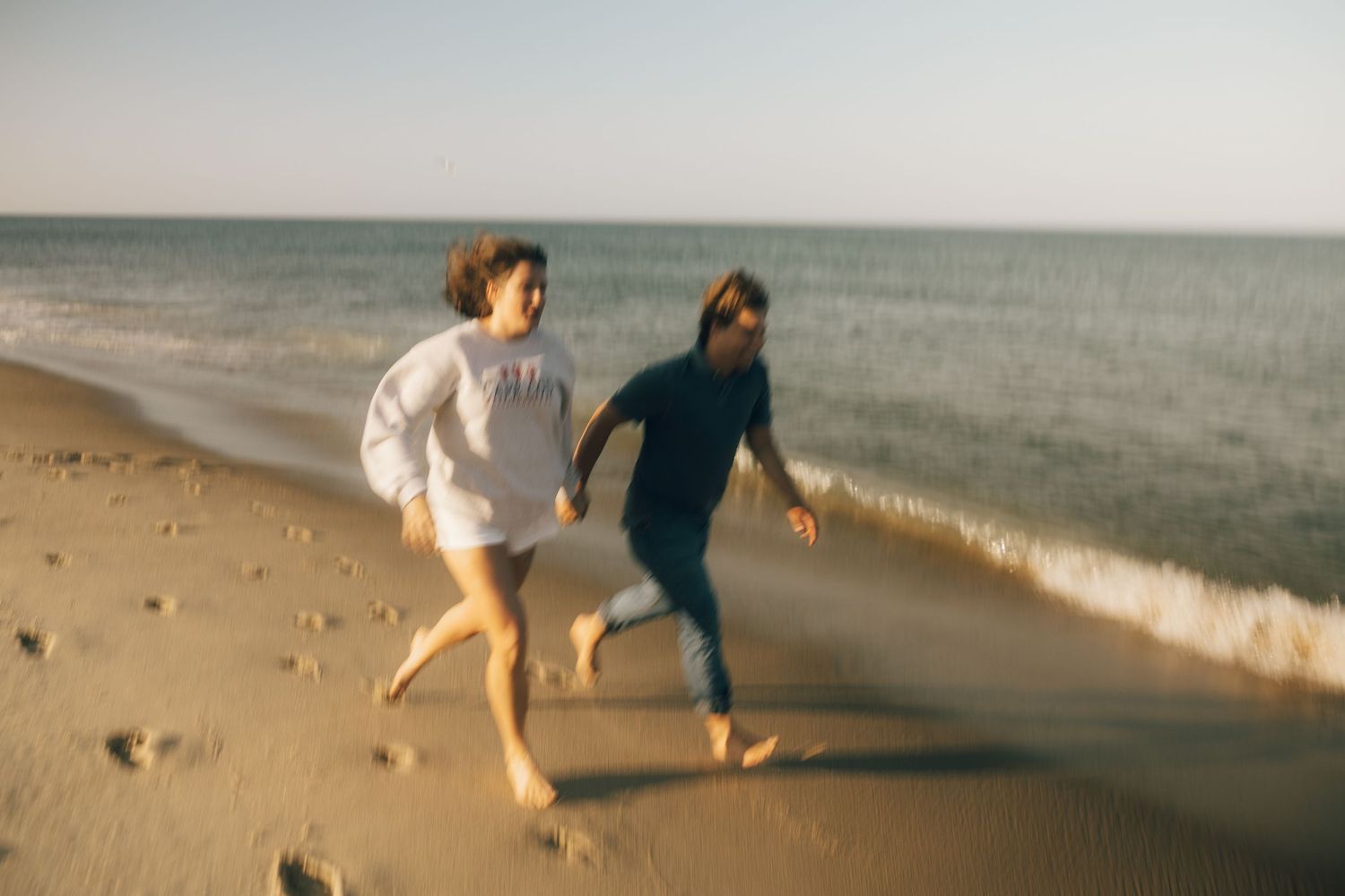 Two figures run along the shoreline with ocean waves in the background.