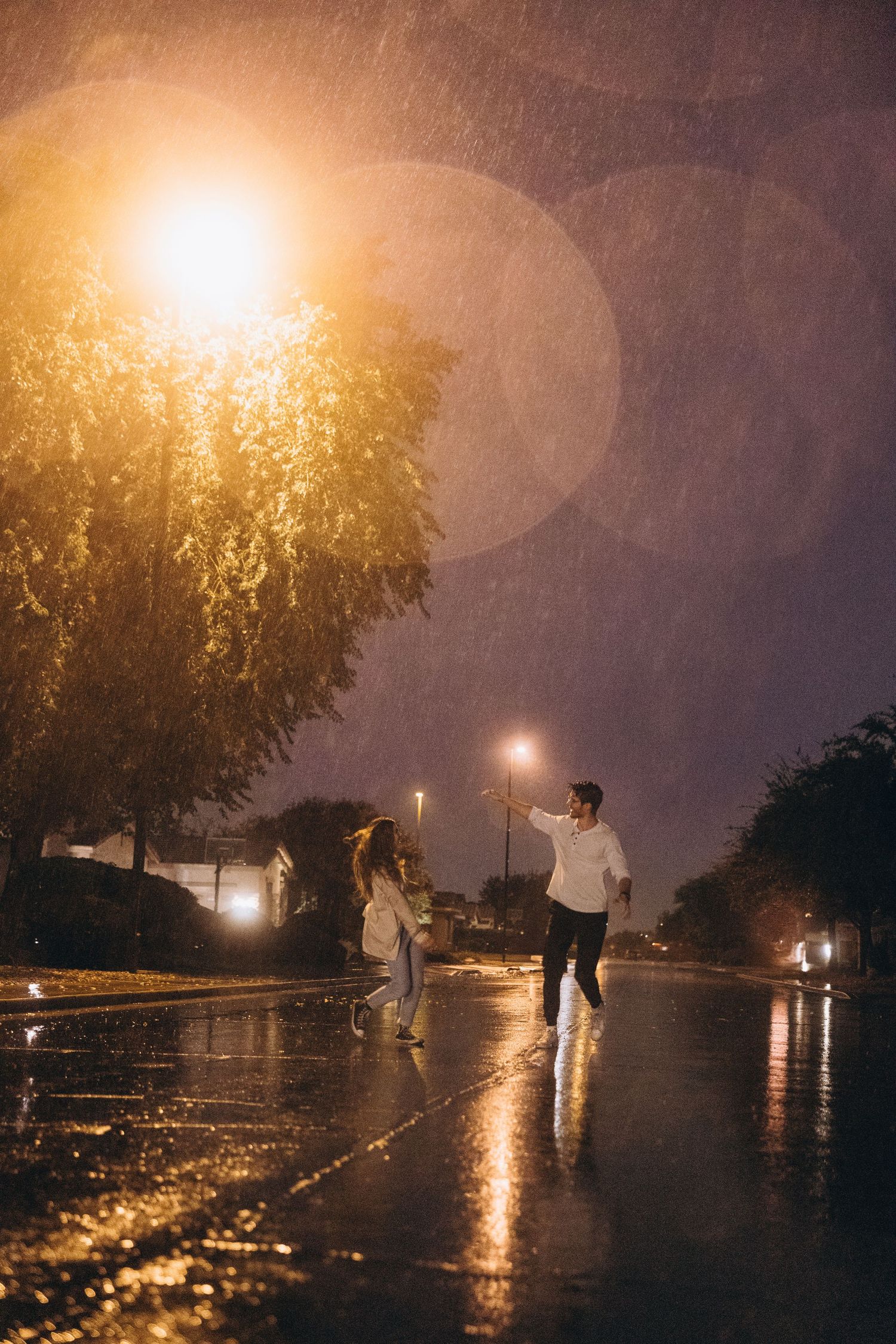 People walking in the rain at night with street lights creating a golden glow and reflections on wet pavement.