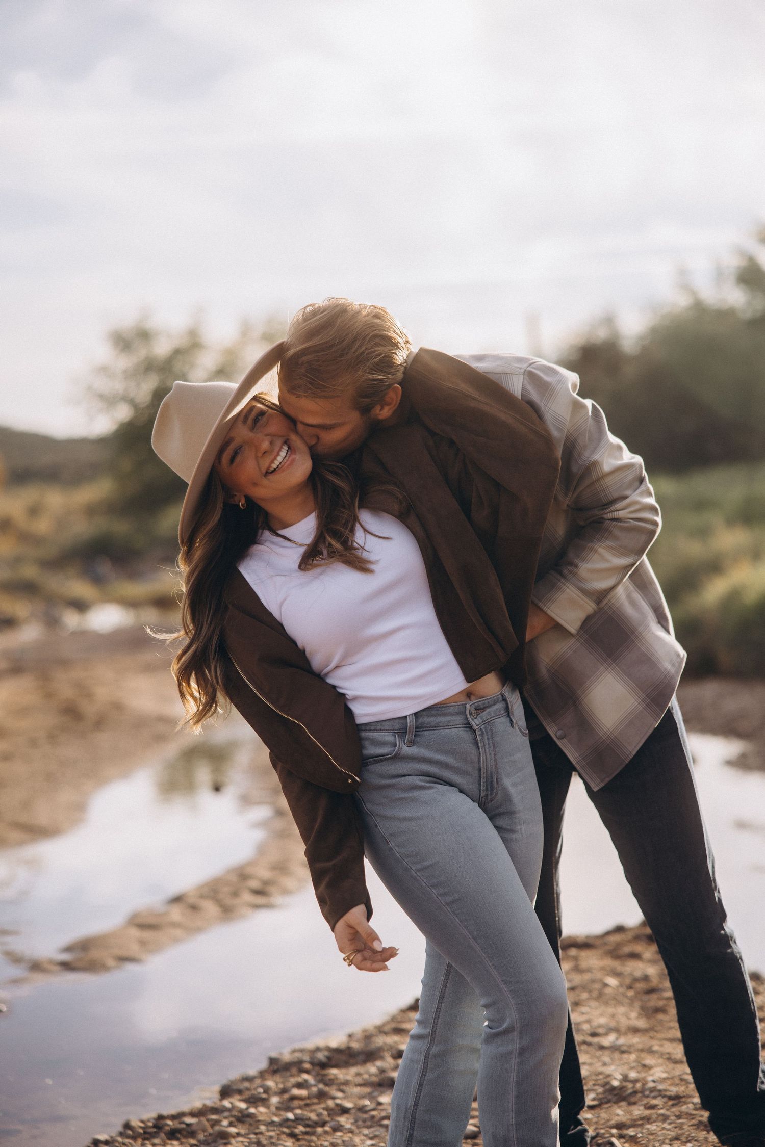 Couple sharing playful laughter moments during a casual outdoor photoshoot by a lake.