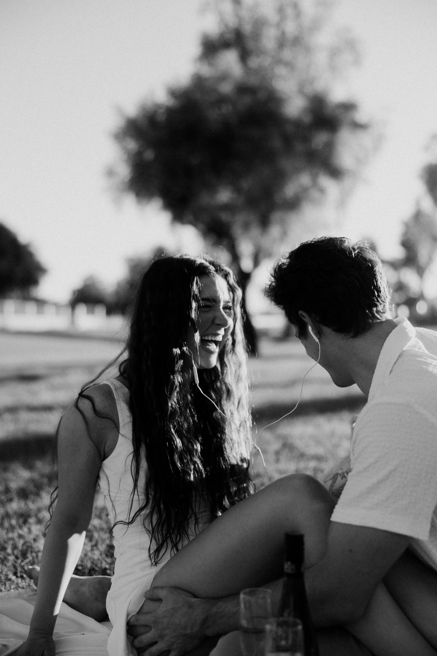 A romantic black and white photo series showing a couple sitting together in a field during golden hour.