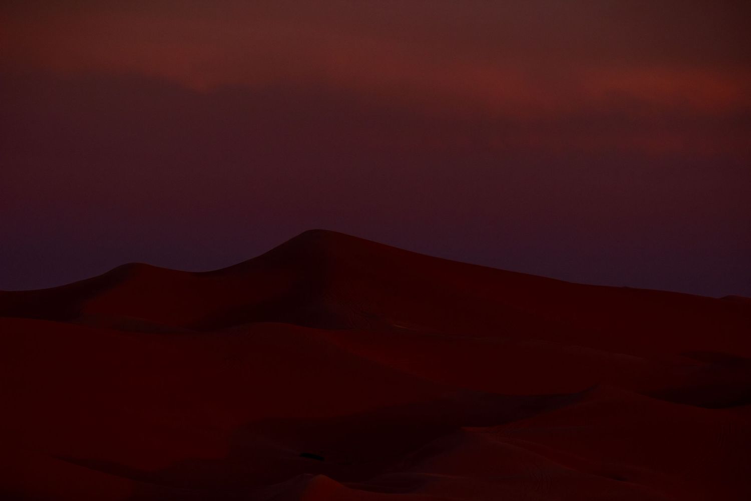 Dark mountain landscape silhouetted against deep red twilight sky.