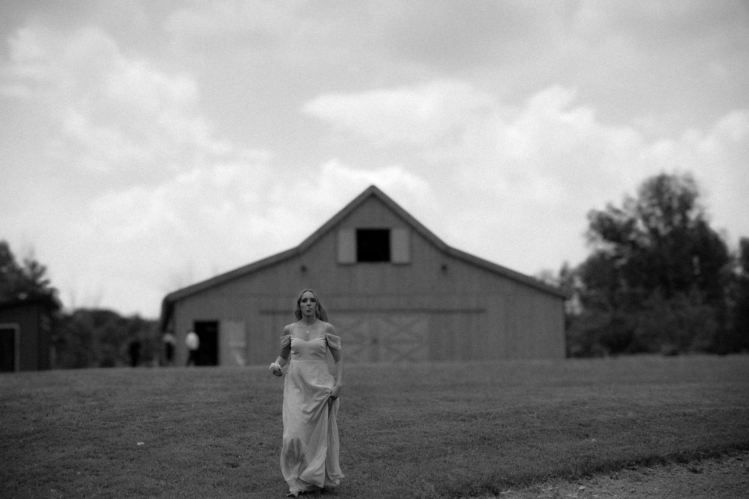 Black and white panoramic view of a rustic barn in a rural field with moody clouds overhead.