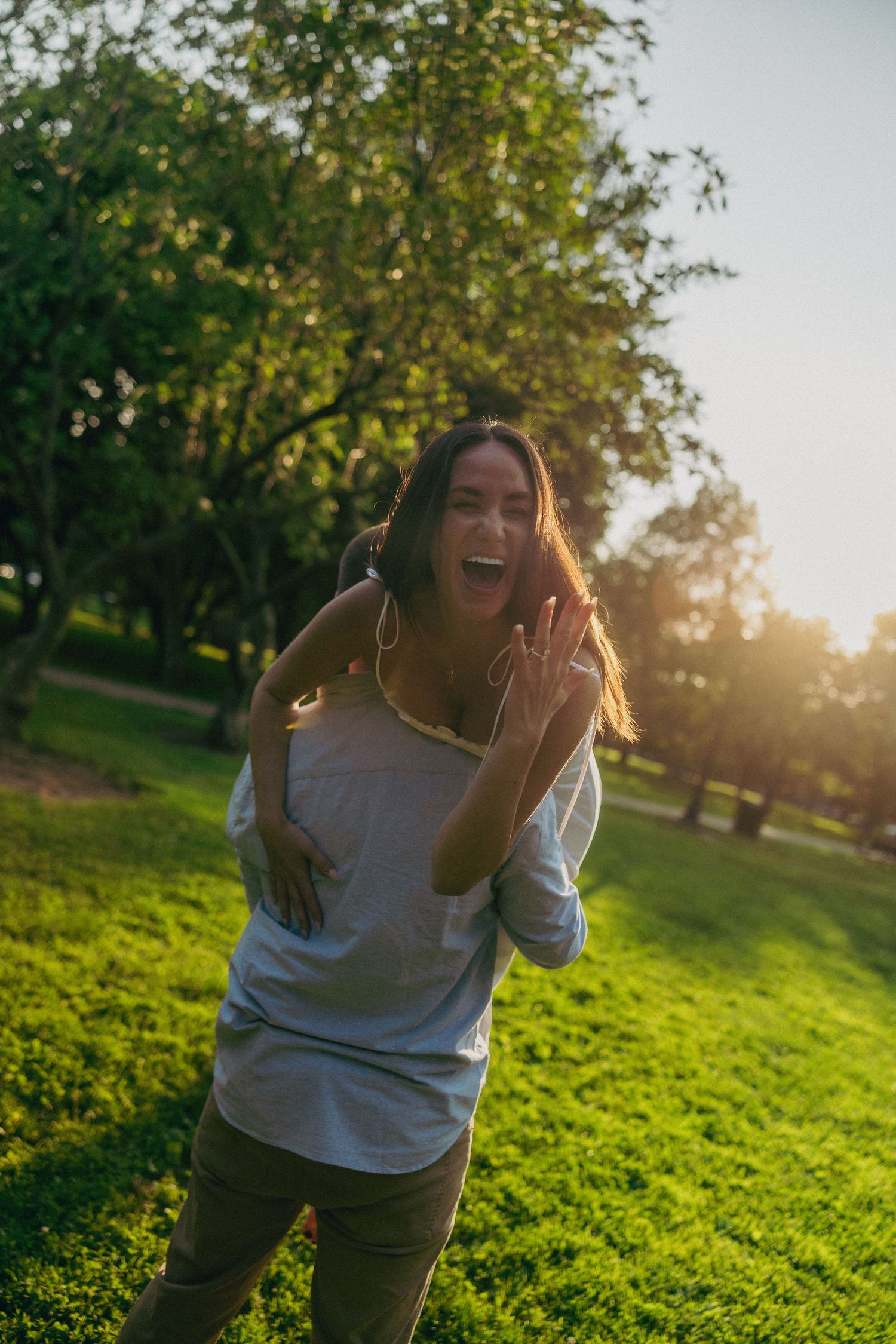 Person laughing joyfully in a sunlit green park.
