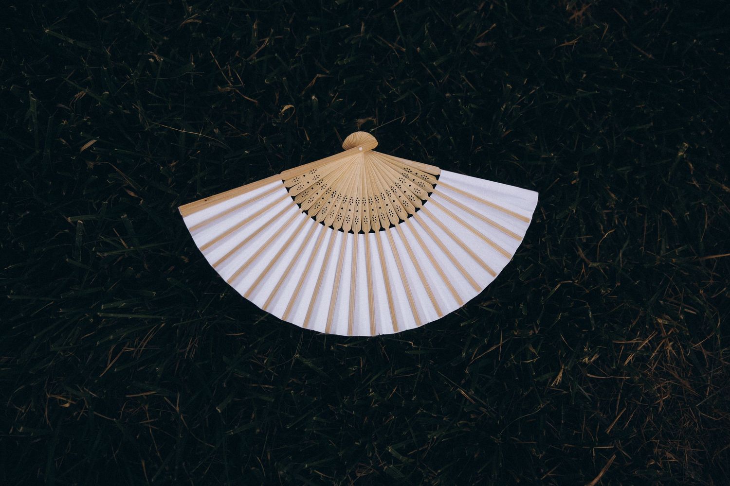 A traditional white folding hand fan with gold accents displayed against a dark background.