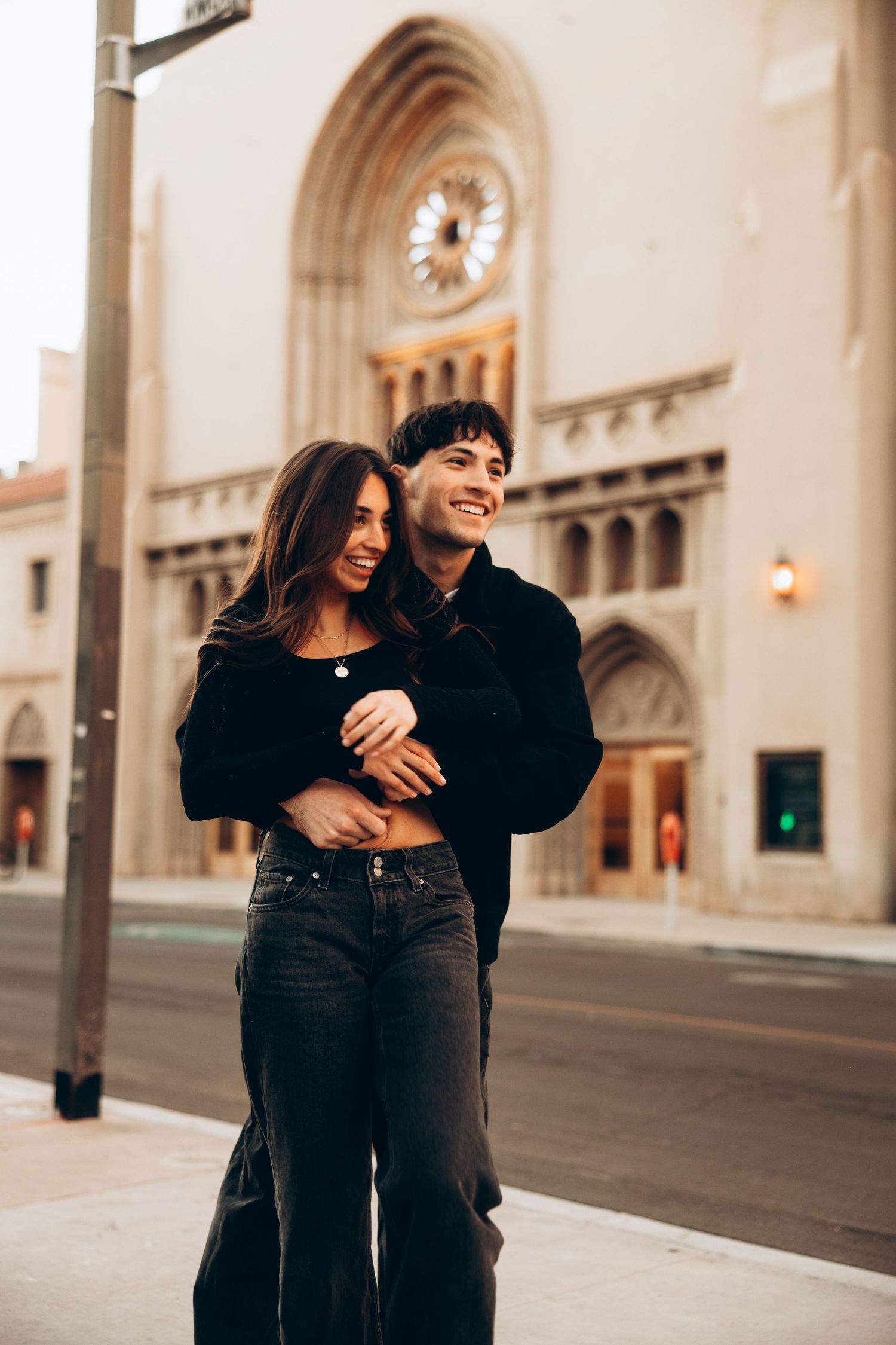 A couple shares a joyful embrace while standing in front of an ornate architectural backdrop with arches and columns.