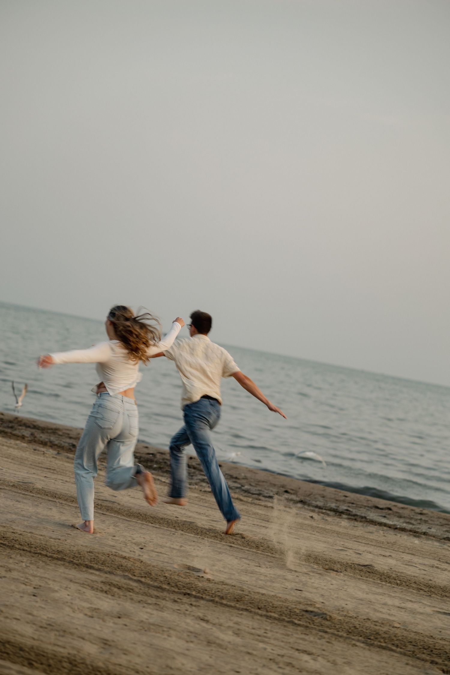 Two people playfully balance on a beach at sunset.