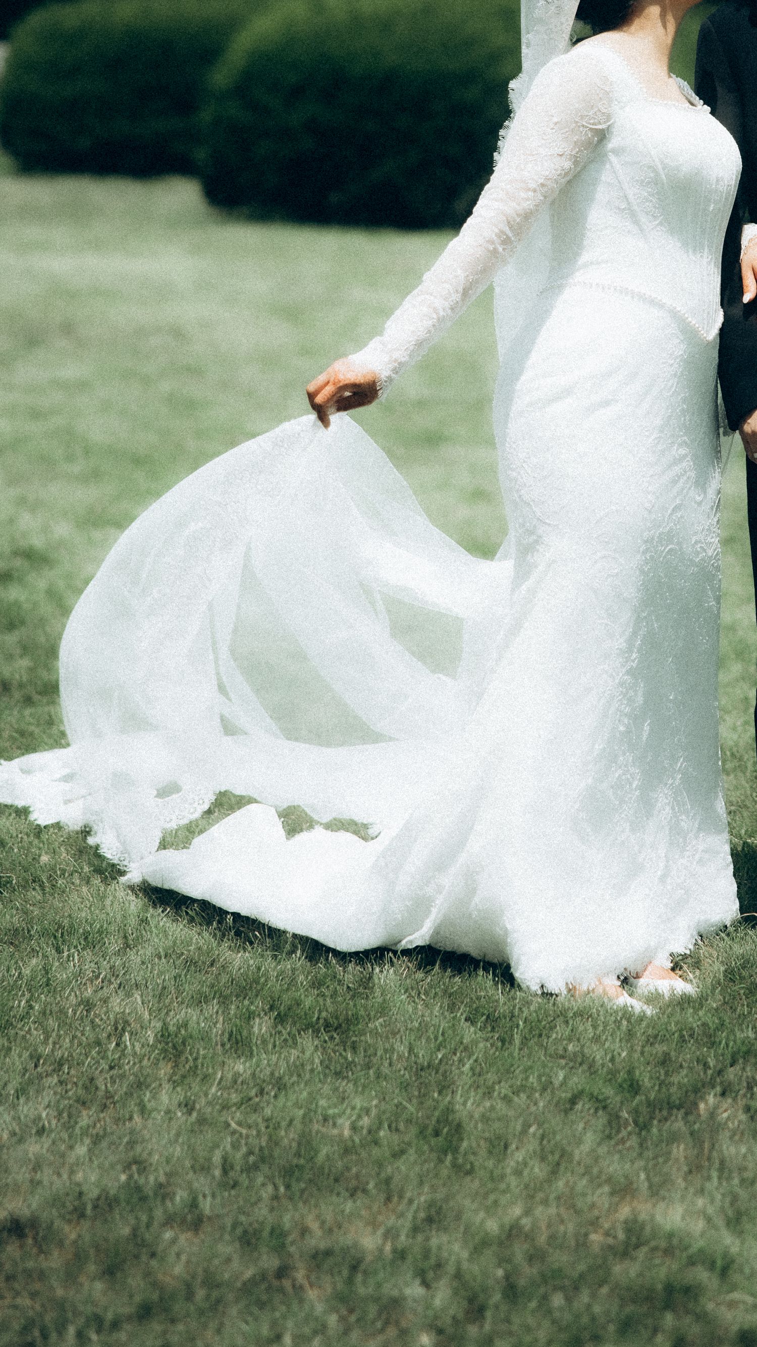 Close-up of flowing white lace wedding dress swirling on grass.