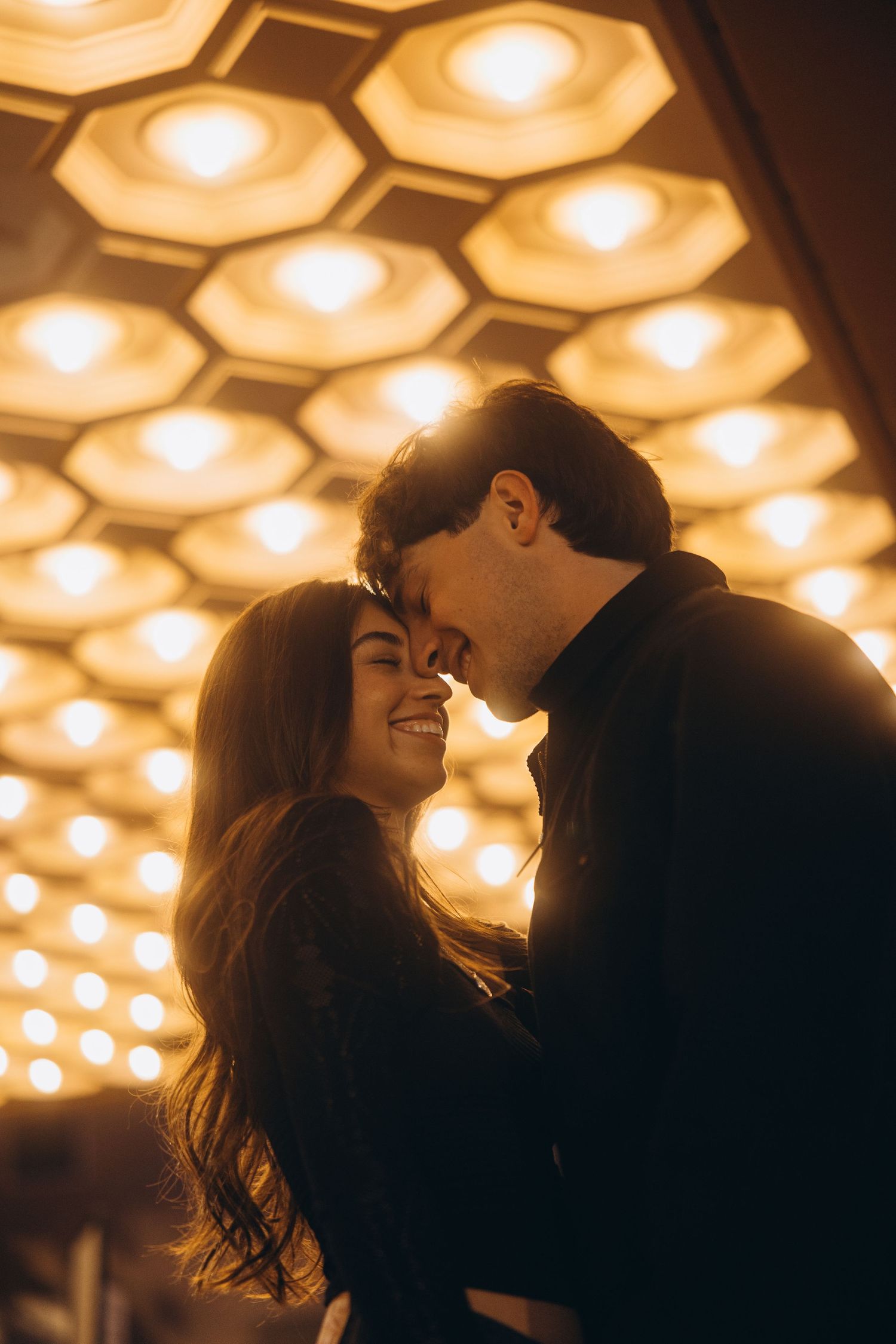 Silhouetted couple sharing an intimate moment under warm honeycomb ceiling lights creating a romantic ambiance.