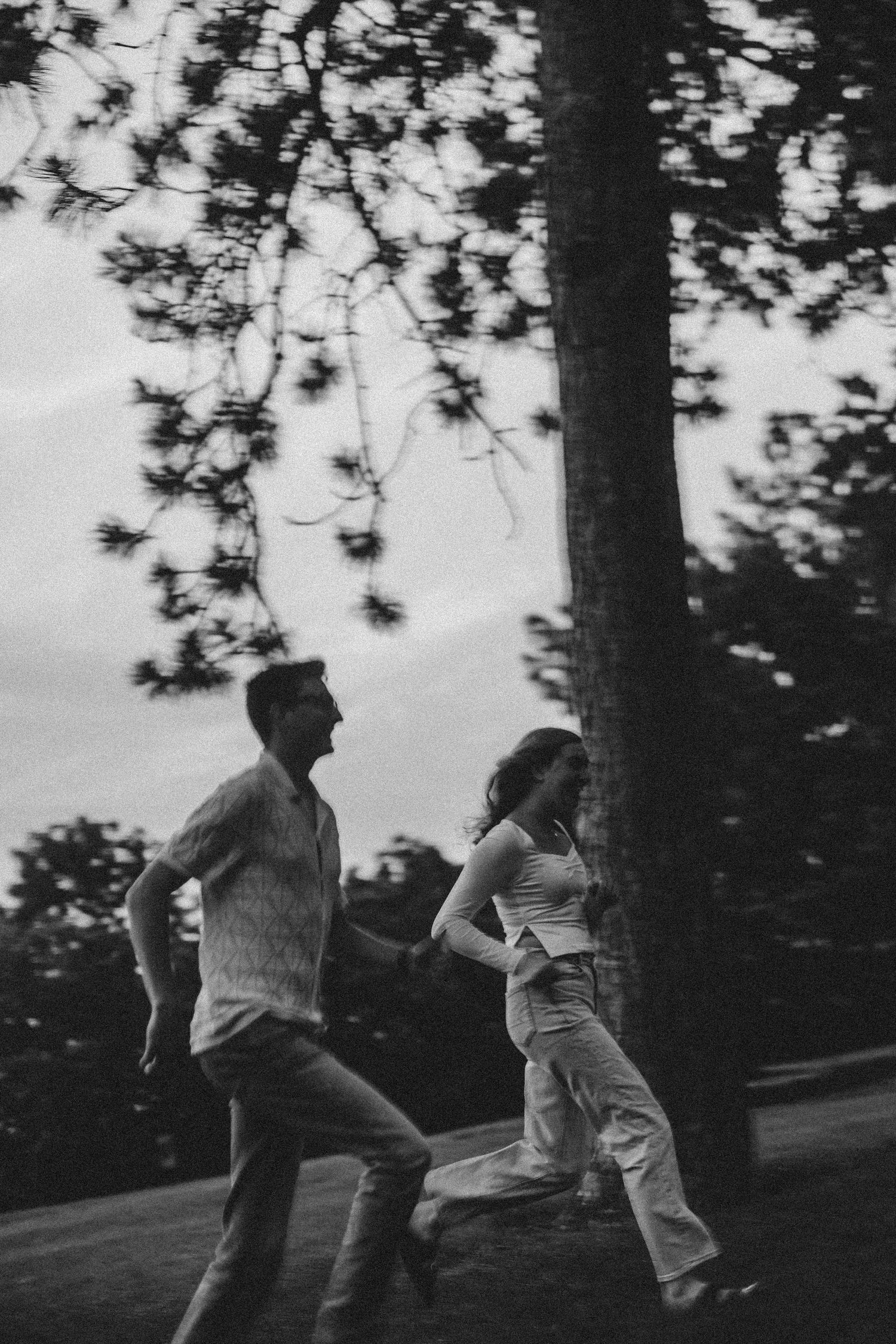 Two people chasing each other through a wooded area in black and white.