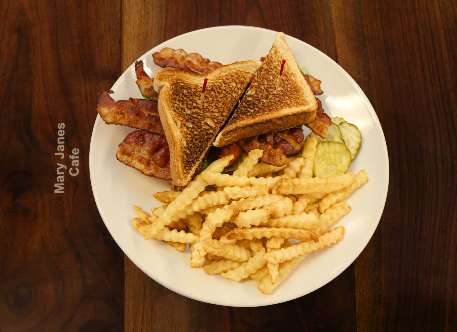 BLT sandwich on toasted bread with crinkle-cut fries and pickle slices on a white plate at Mary Janes Cafe.