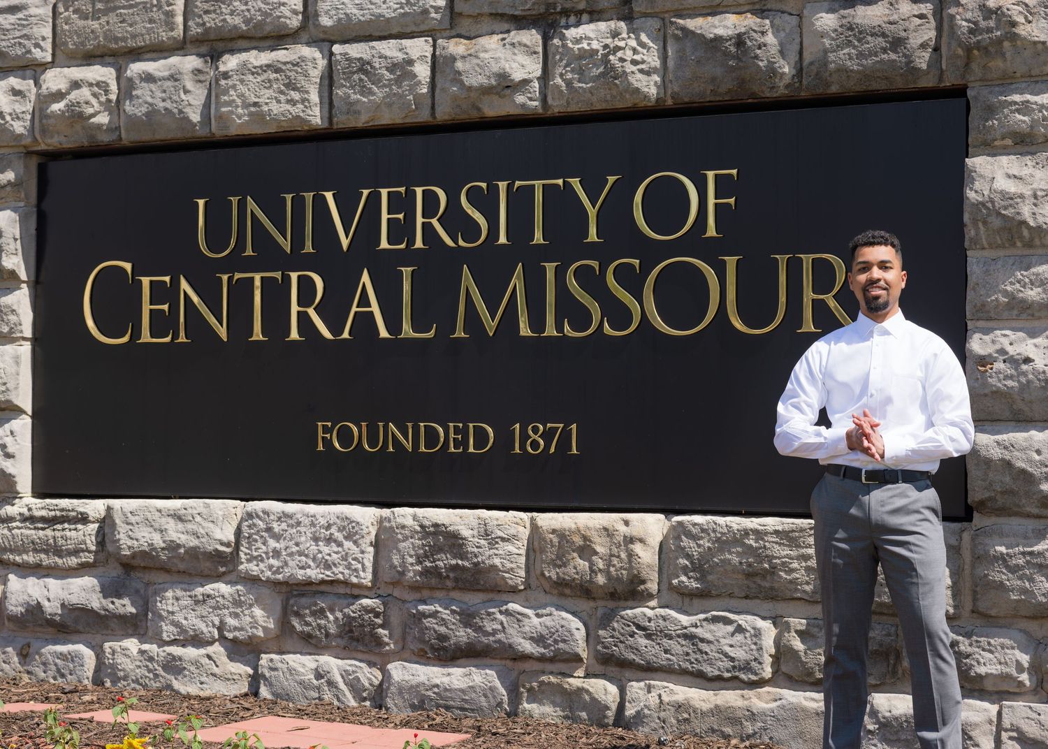 Man posing in front of University of Central Missouri Founded 1871 stone sign on sunny day.