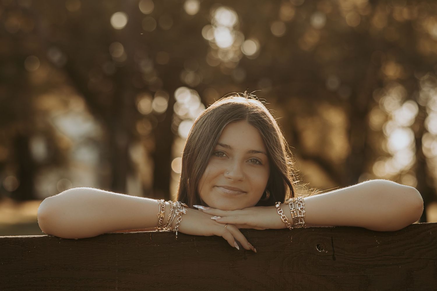 A person rests their arms on a wooden fence during golden hour with sunlit bokeh in the background.