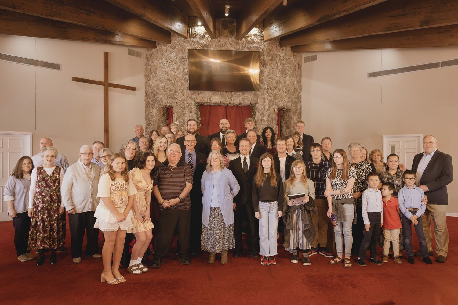 Large group of people posing together inside a church with a cross and stone fireplace backdrop.