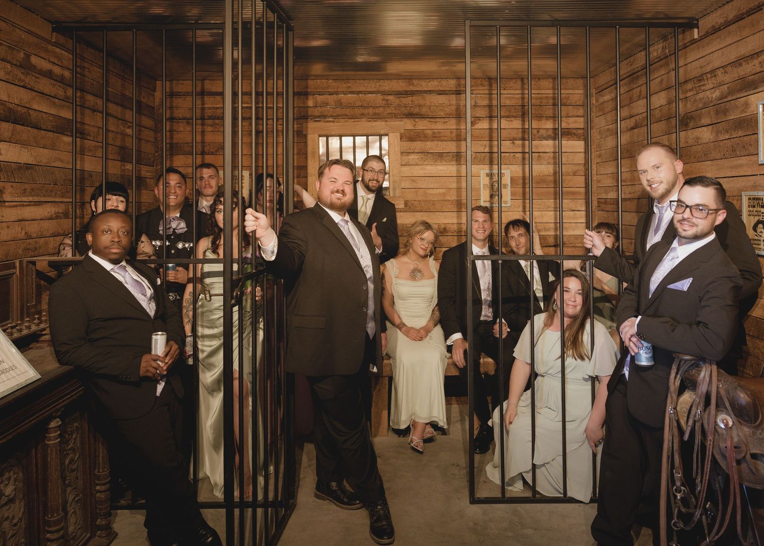 Wedding party posing in a rustic wooden jail cell set, bride and groom centered with groomsmen and bridesmaids.