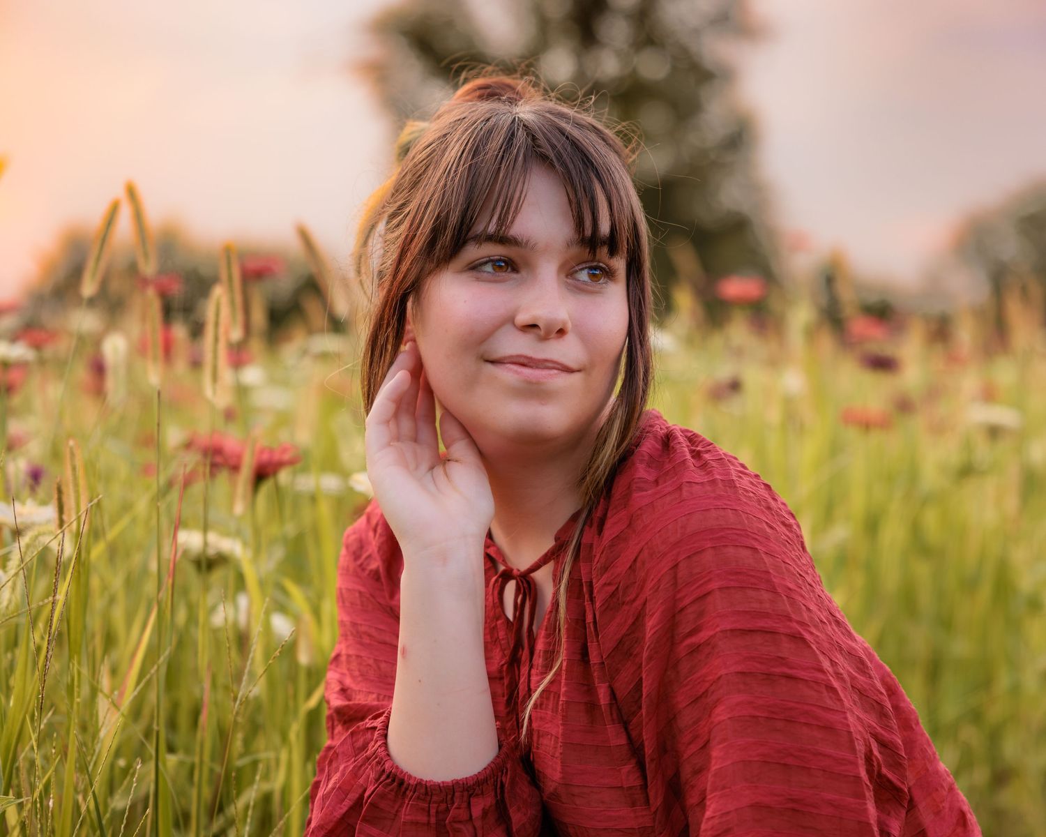 Young woman in red dress sitting in a wildflower field at golden hour sunset.