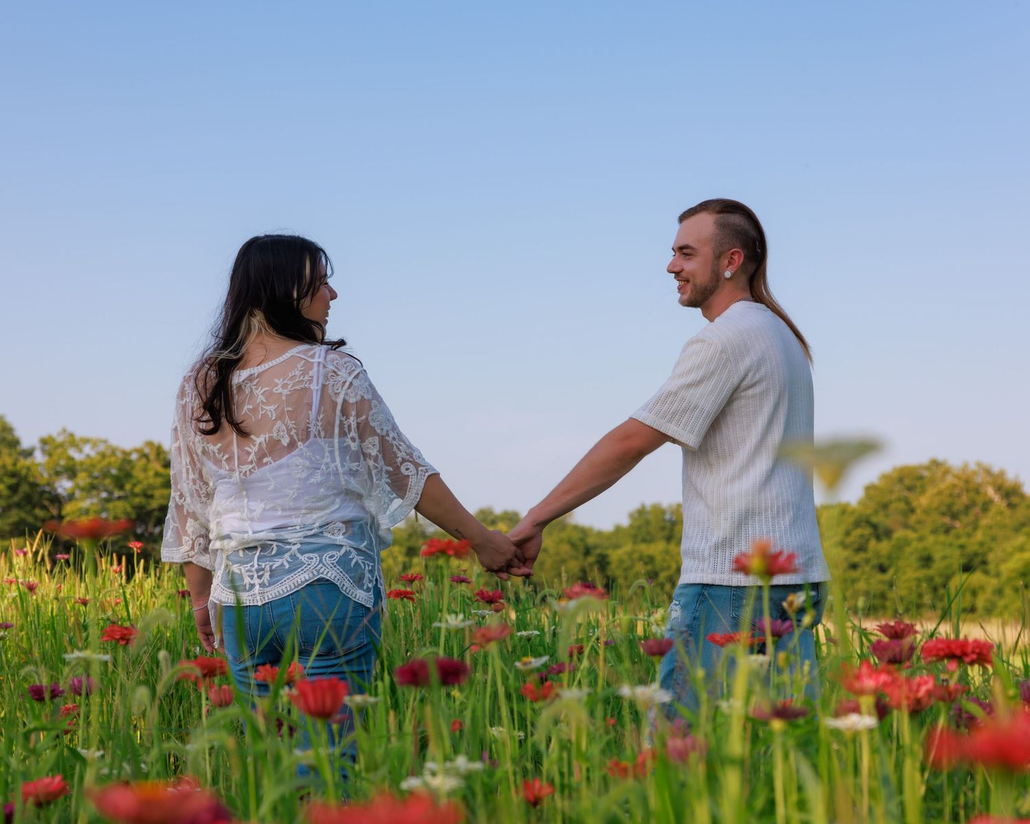 Couple holding hands in a vibrant poppy field under a clear blue sky on a sunny day.