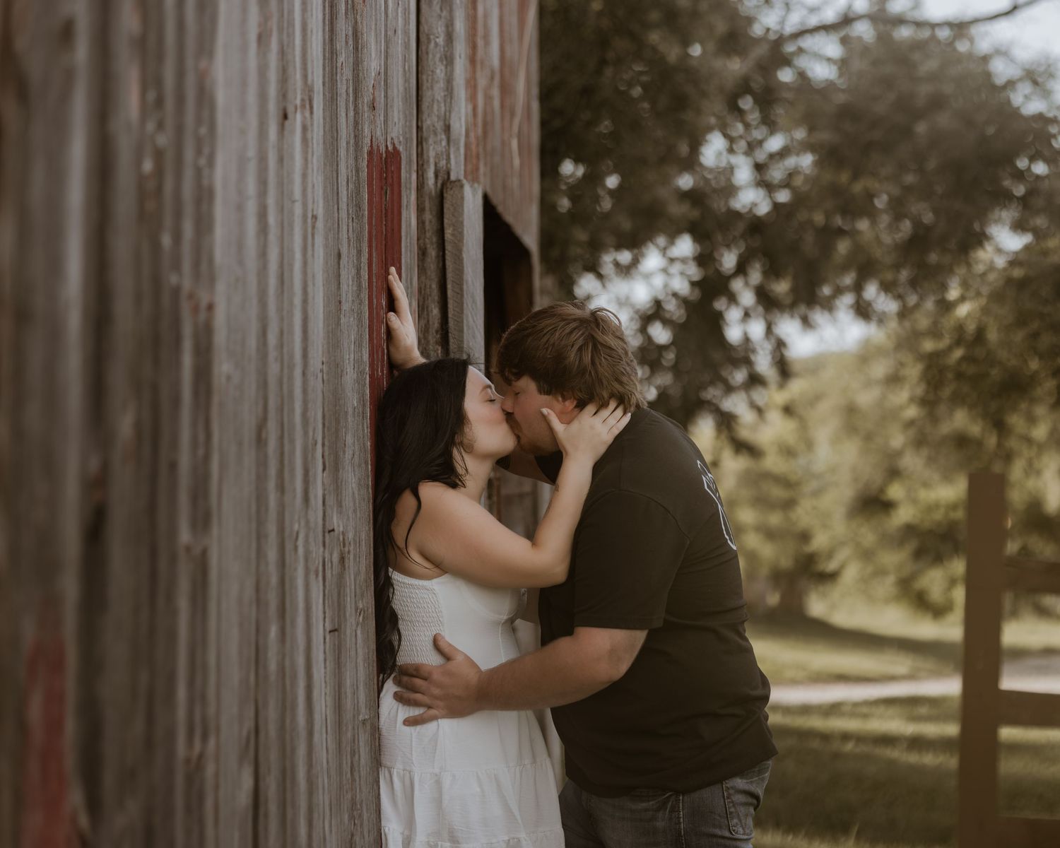 Couple sharing a romantic kiss against a rustic barn wall outdoors.