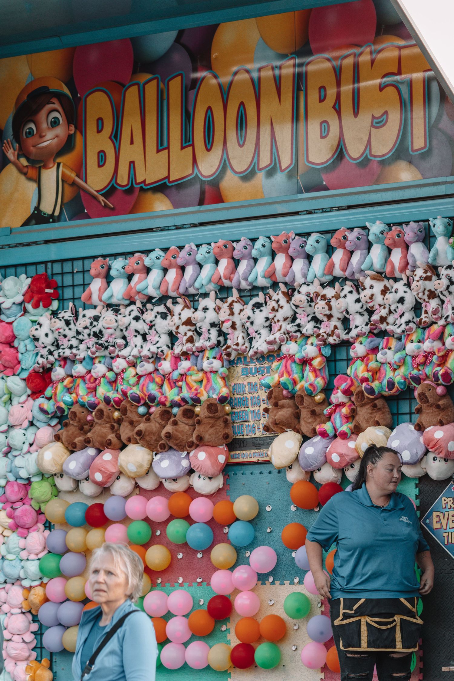 Colorful carnival game booth decorated with pink and orange balloons and stuffed animal prizes.