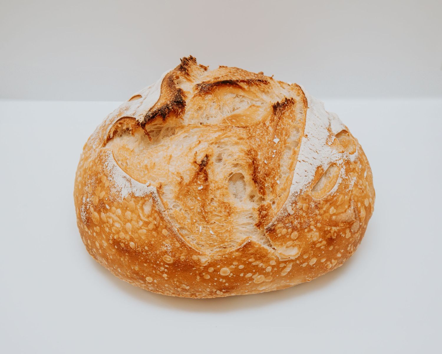 A freshly baked artisan sourdough bread loaf shown from multiple angles against a light background.