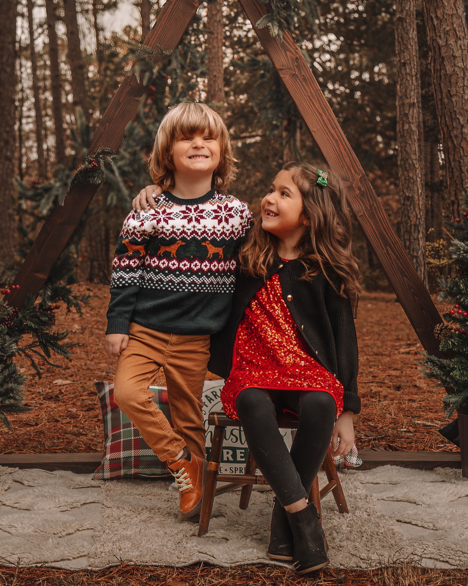 Two children sitting on a stone bench in autumn woods wearing festive sweaters and seasonal outfits.