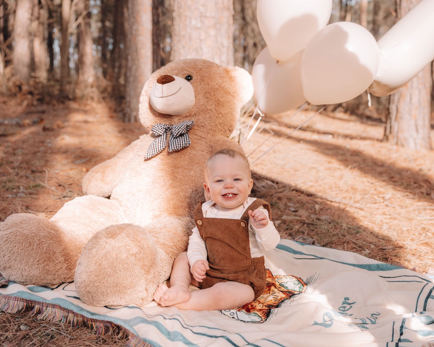 Outdoor forest scene with a large teddy bear and blanket arranged for a photo session.