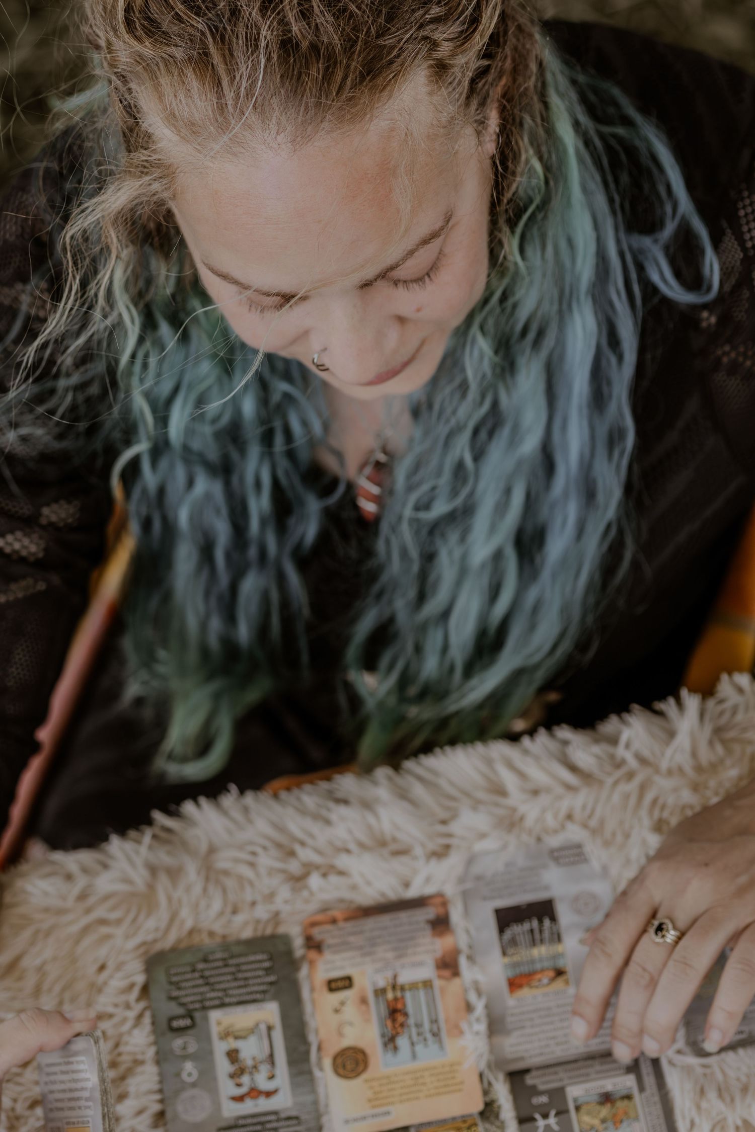 Person with blue hair examining vintage books and papers on a white surface.