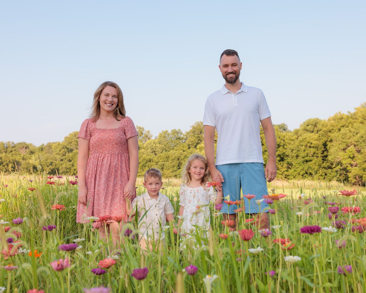 Family of four posing in a colorful wildflower field on a sunny day, smiling together outdoors.