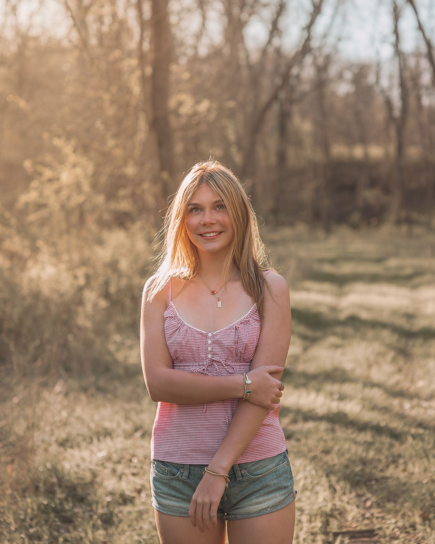 Smiling young blonde woman in pink camisole standing in golden sunlit meadow.