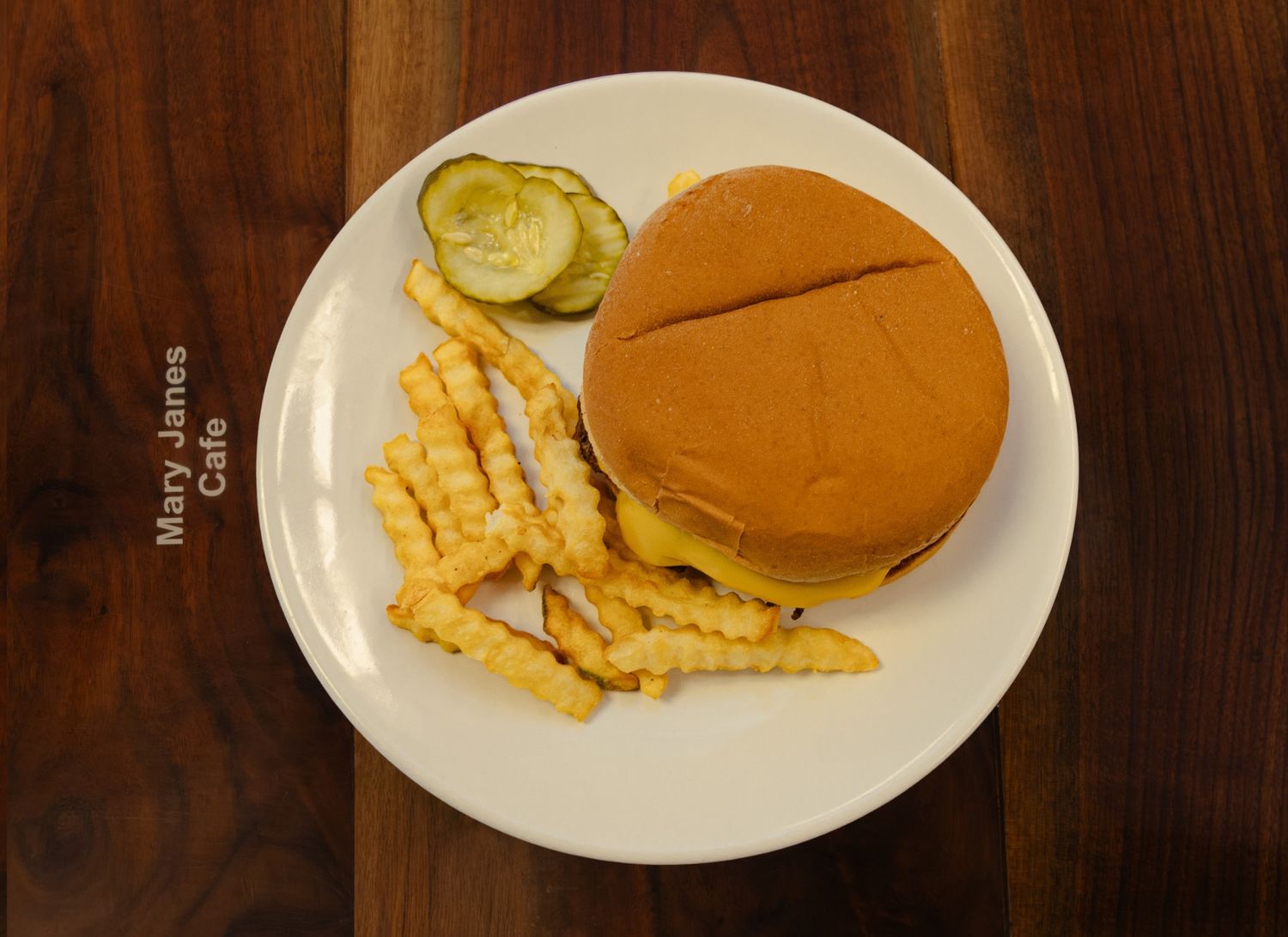 Cheeseburger with crinkle-cut fries and pickle slices on a white plate at Mary Janes Cafe.