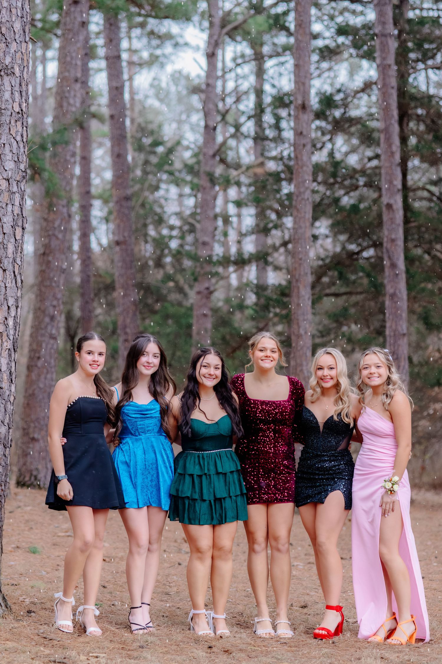 Group wearing coordinated outfits standing in a row showing their footwear in a pine forest setting.