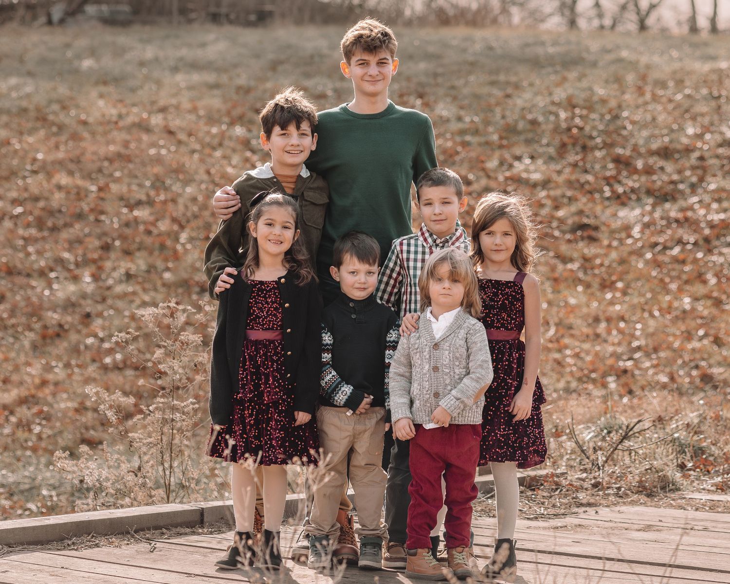 A group poses together outdoors in coordinated fall outfits against a backdrop of autumn leaves and foliage.