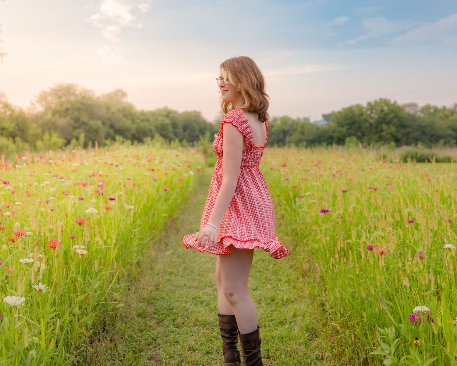 A young girl in a pink dress and brown boots stands in a vibrant wildflower field at golden hour.