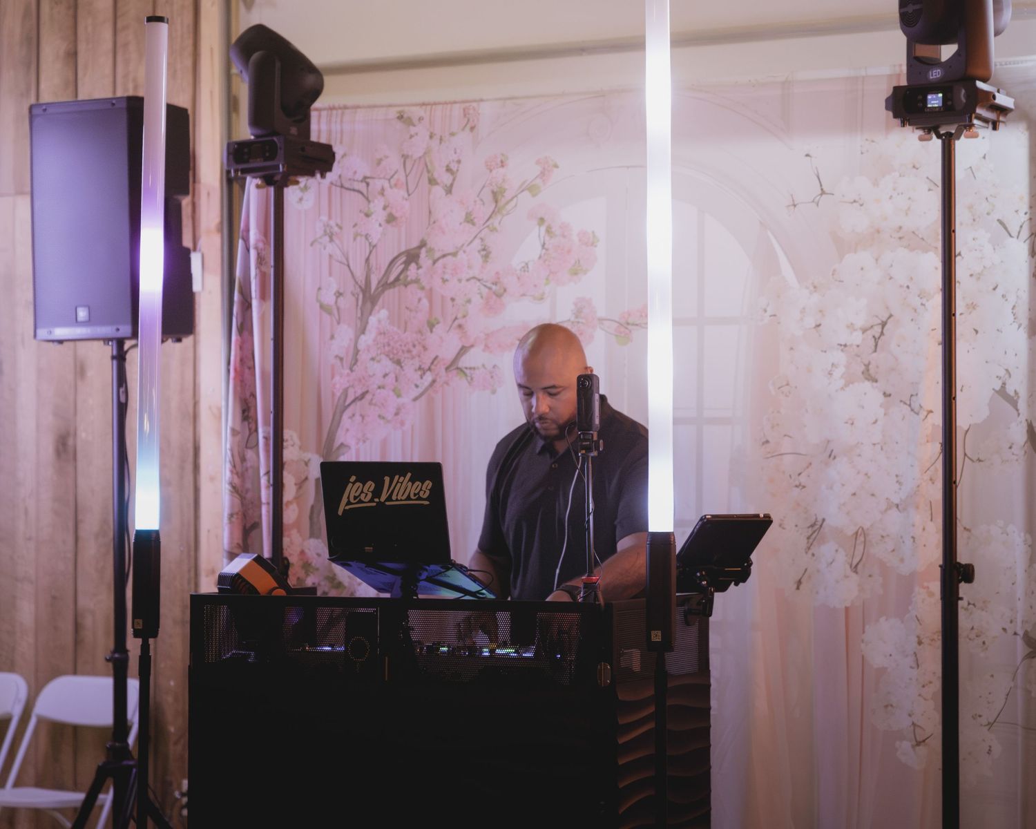 DJ wearing headphones operates turntables at wedding reception setup with speakers and lighting equipment.