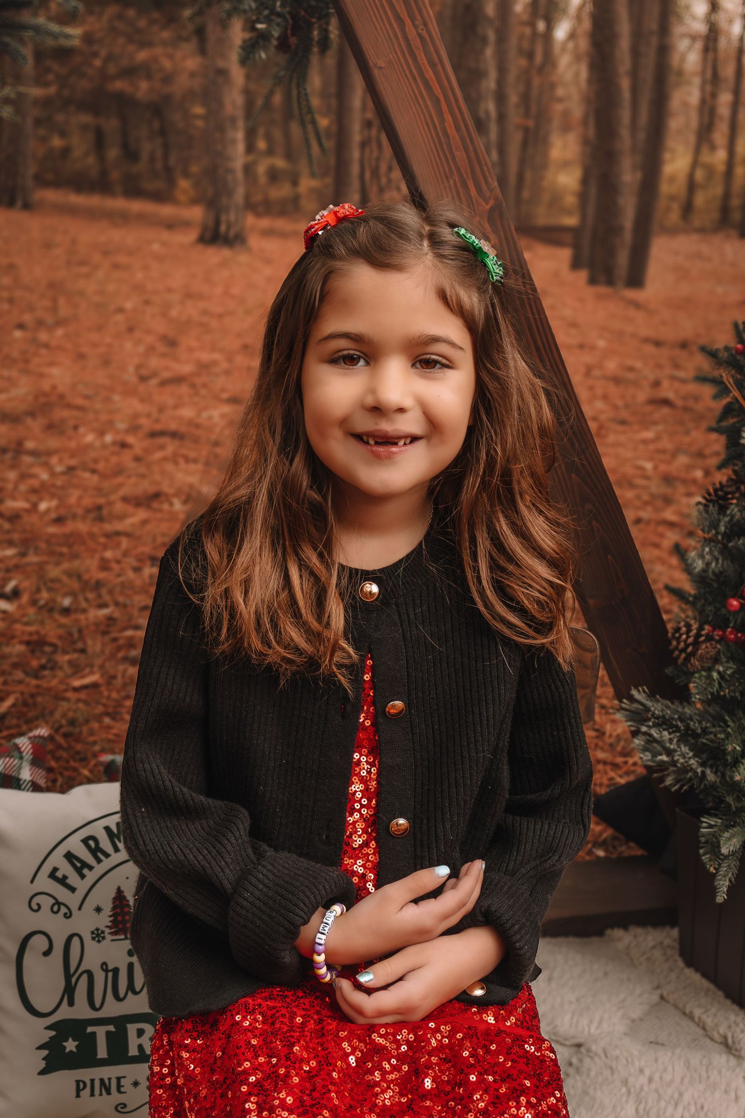 A child in a black sweater and red polka dot dress sits on a cushion in an autumn forest setting.