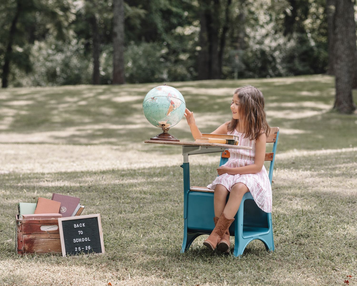Vintage-style outdoor photoshoot setup featuring a blue toy car, globe, and wooden crates on grass.