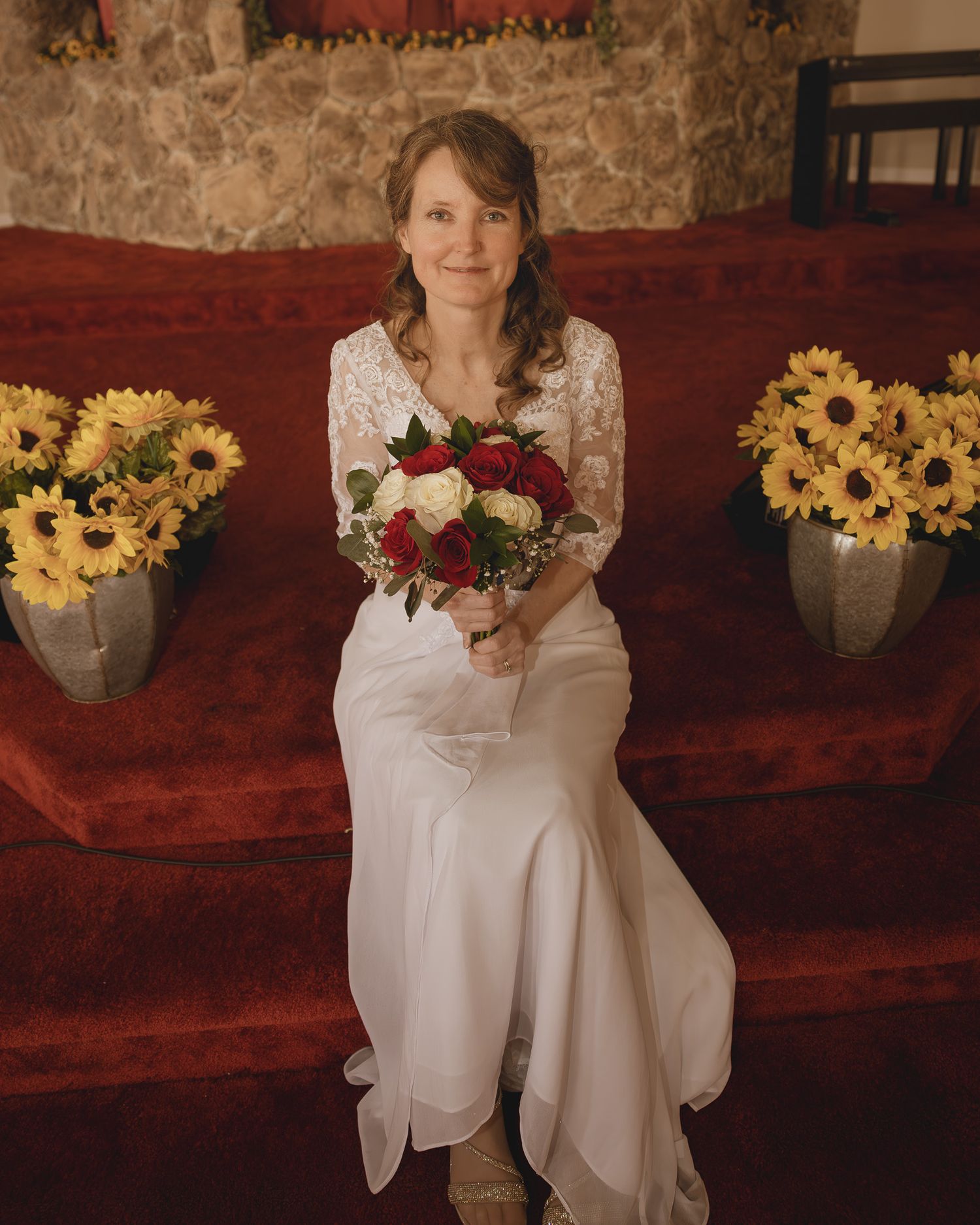 White wedding dress and sunflower bouquet arrangements against rustic red wooden wall create elegant rustic decor.
