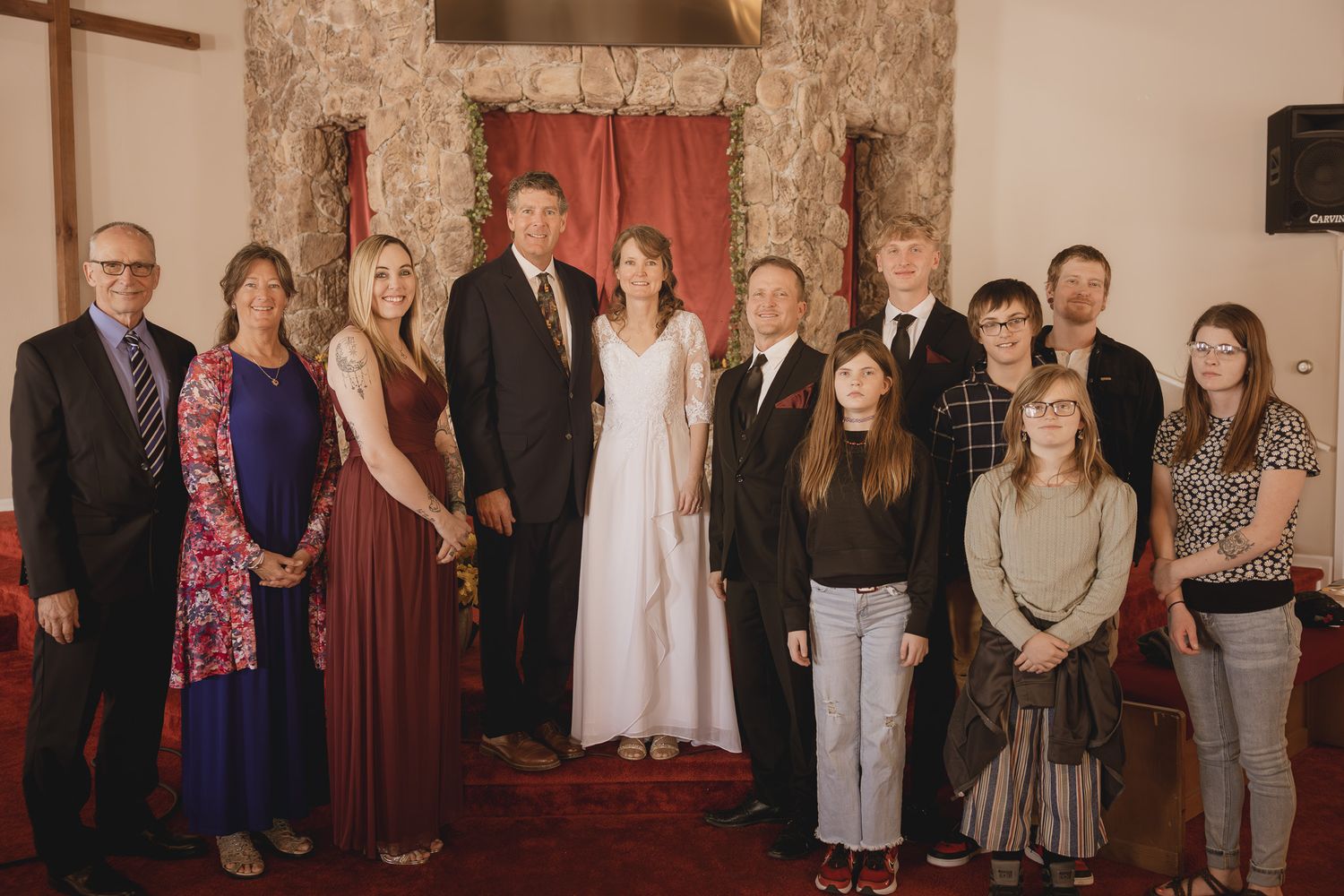 A formal group photo taken in front of a stone wall and red curtain in a church setting.