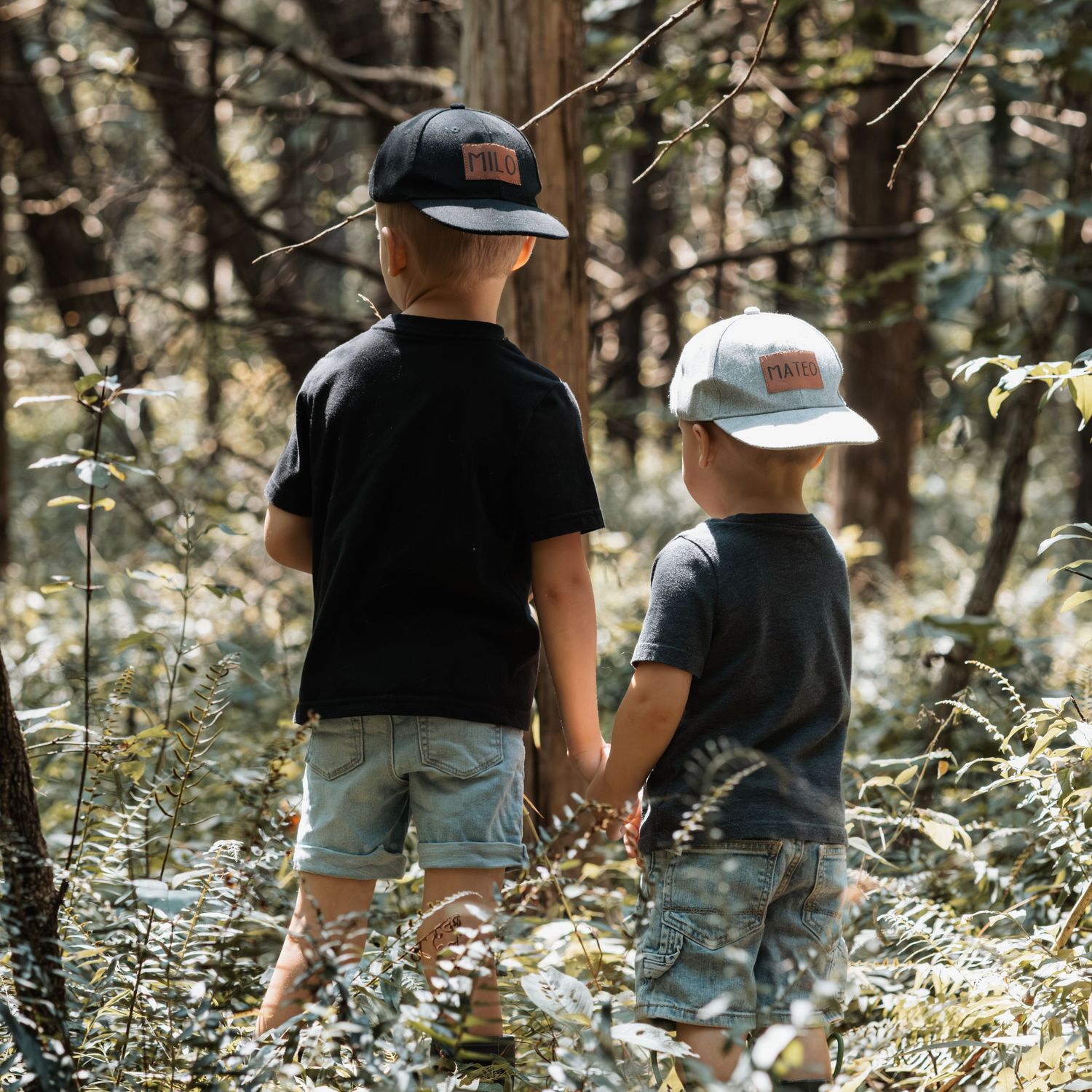 Two children in baseball caps exploring a forest together during a summer adventure.