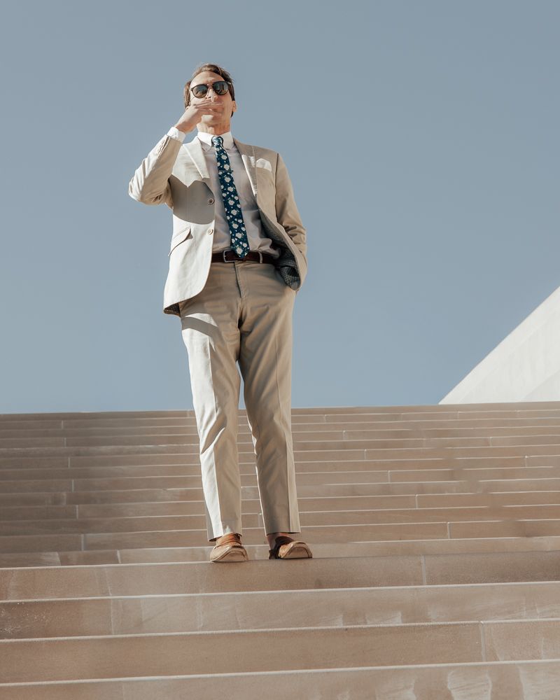 Person in beige suit and sunglasses descending concrete steps against blue sky background.