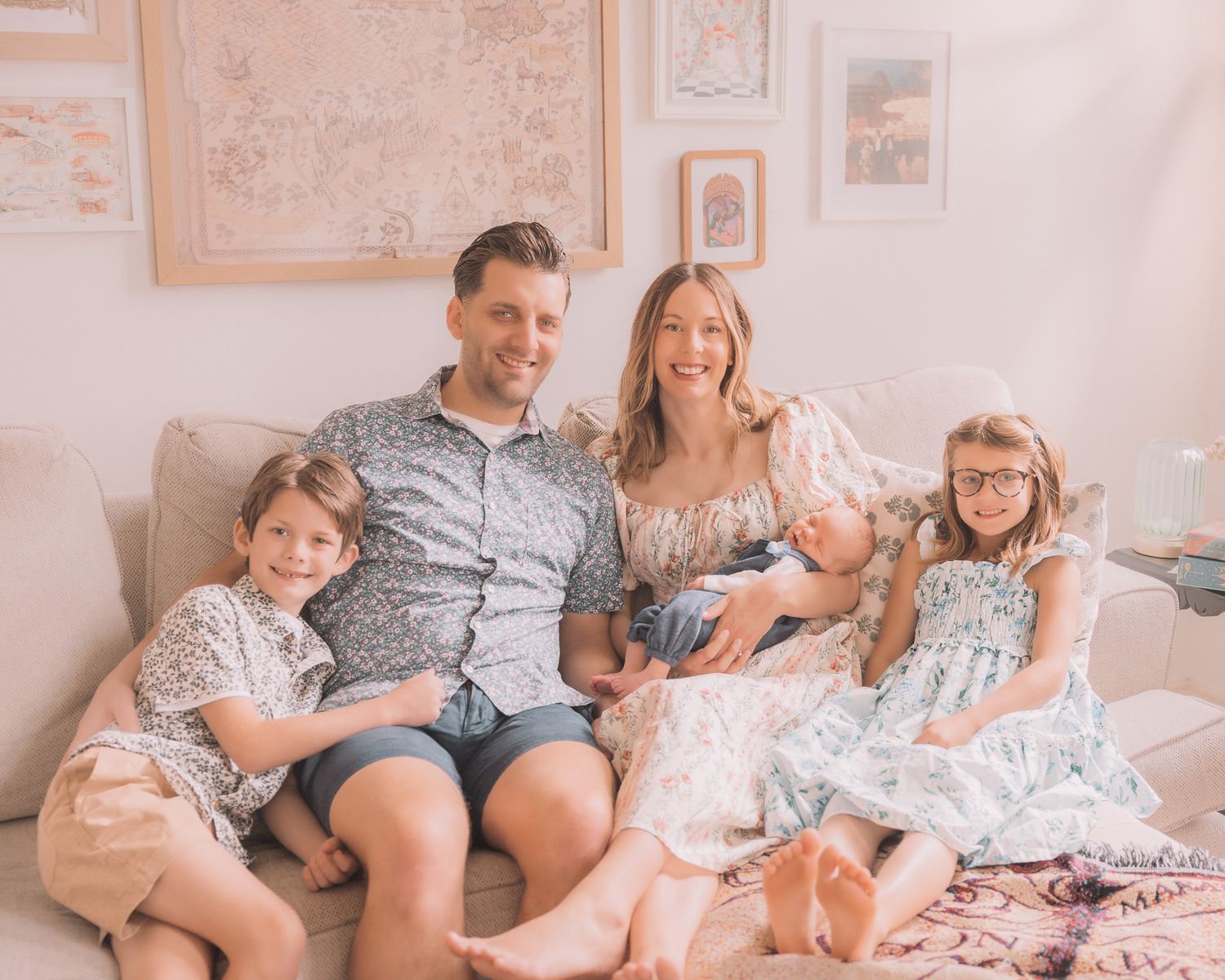 Happy family of five sitting together on a couch, parents smiling with three young children in a bright, cozy room.