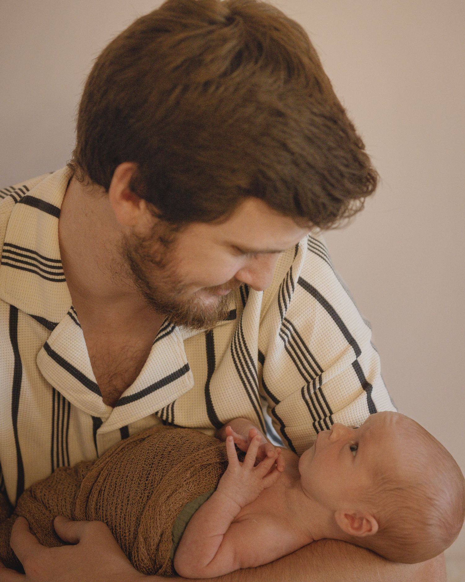 Bearded father tenderly holding his swaddled newborn baby close.