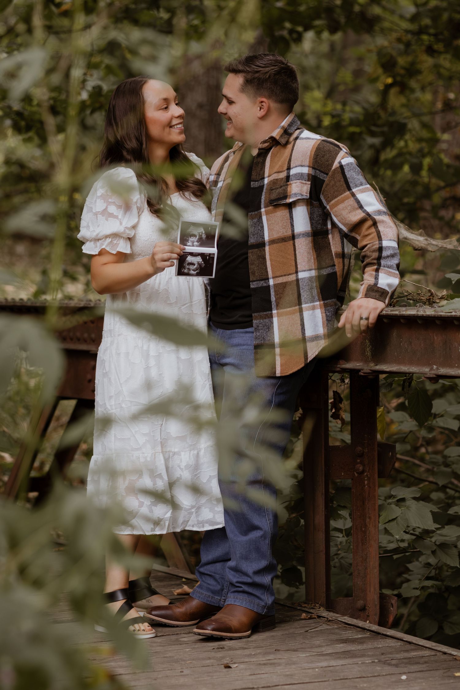 A couple shares a romantic moment on a wooden bridge surrounded by lush greenery in a natural setting.