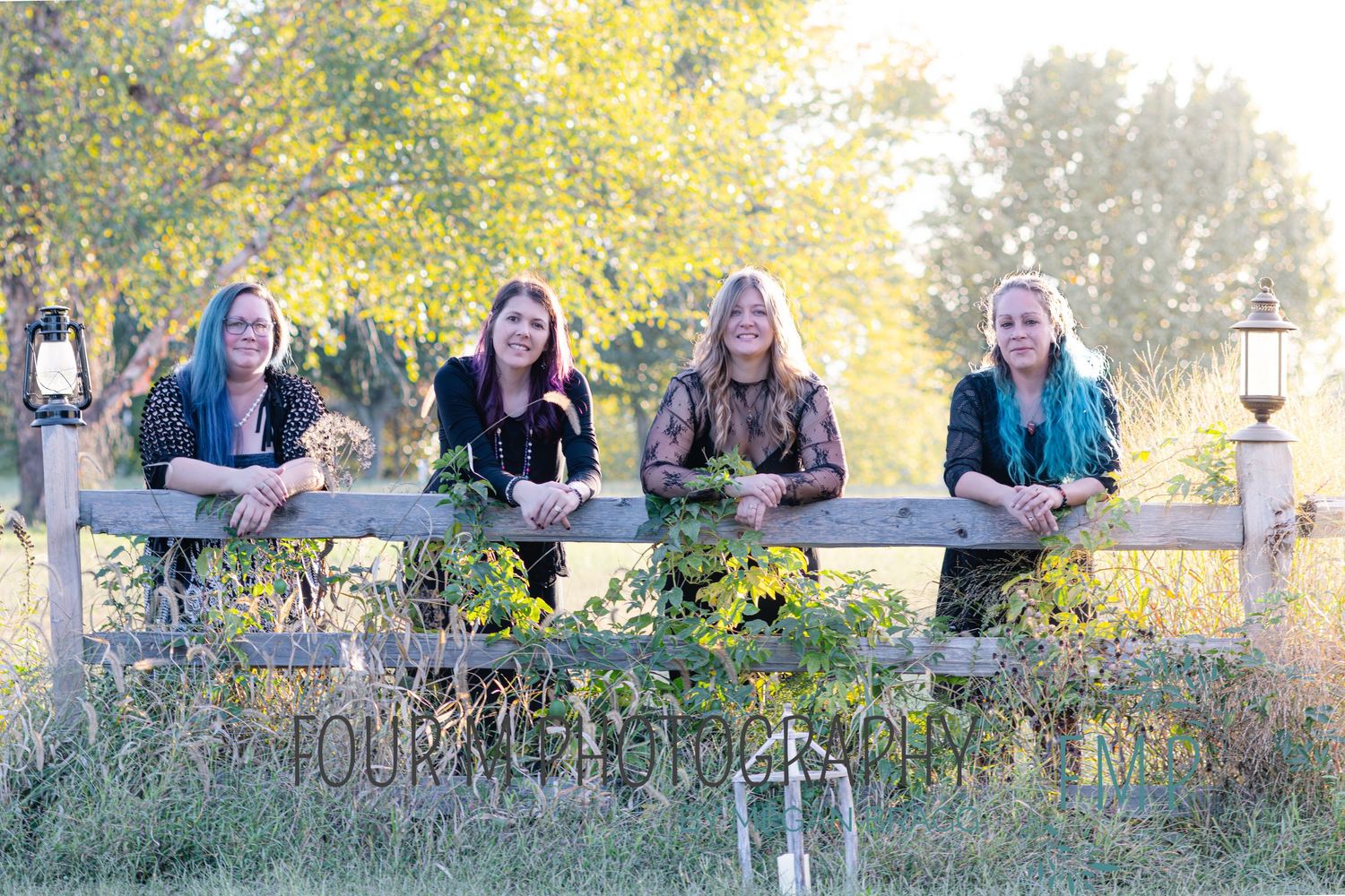 A group sits together on a rustic wooden fence surrounded by autumn foliage and lantern decorations in an outdoor setting.