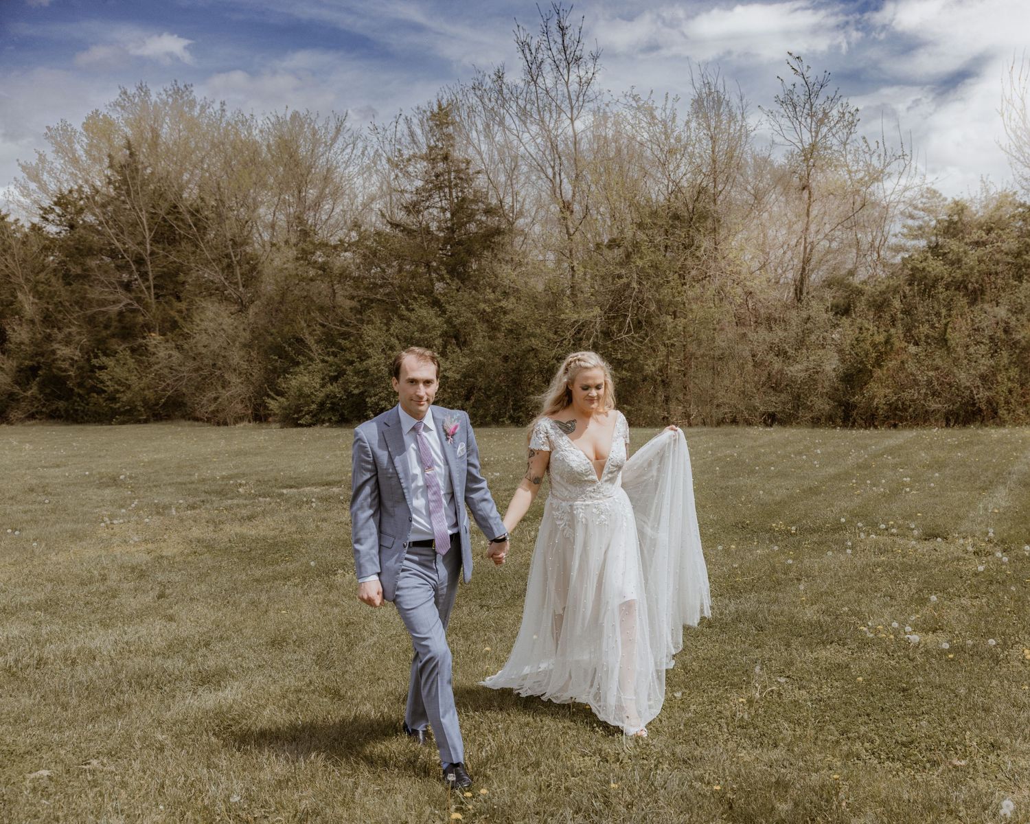 Smiling bride and groom running through a lush green field on their wedding day.