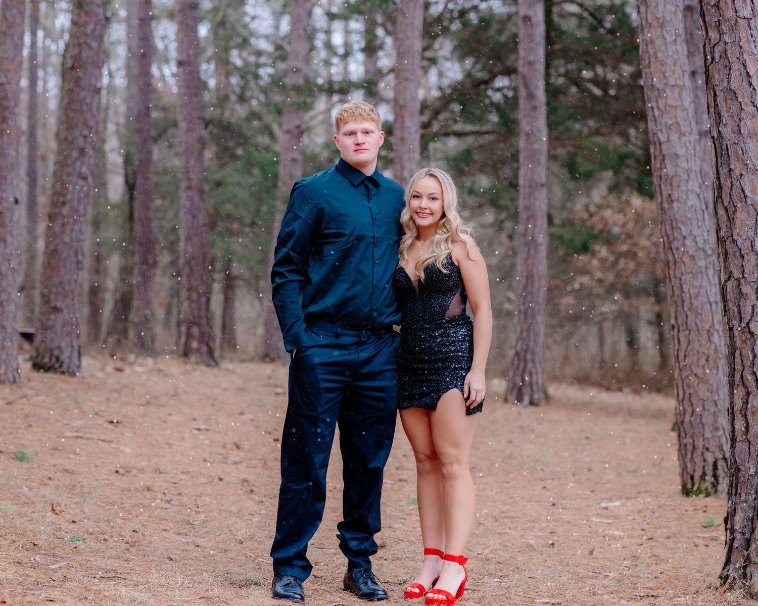 A couple walks through a pine forest holding hands during an outdoor photo session.