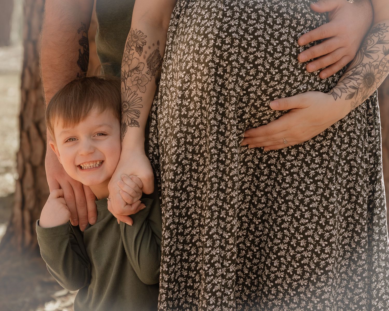 A smiling boy leans on his tattooed parents, one visibly pregnant, in a warm family maternity photo shoot.