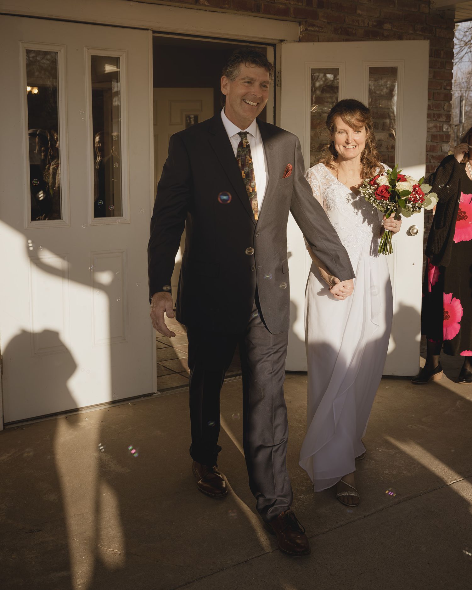 Wedding party members walk down a sunlit hallway in formal attire during a joyful celebration.