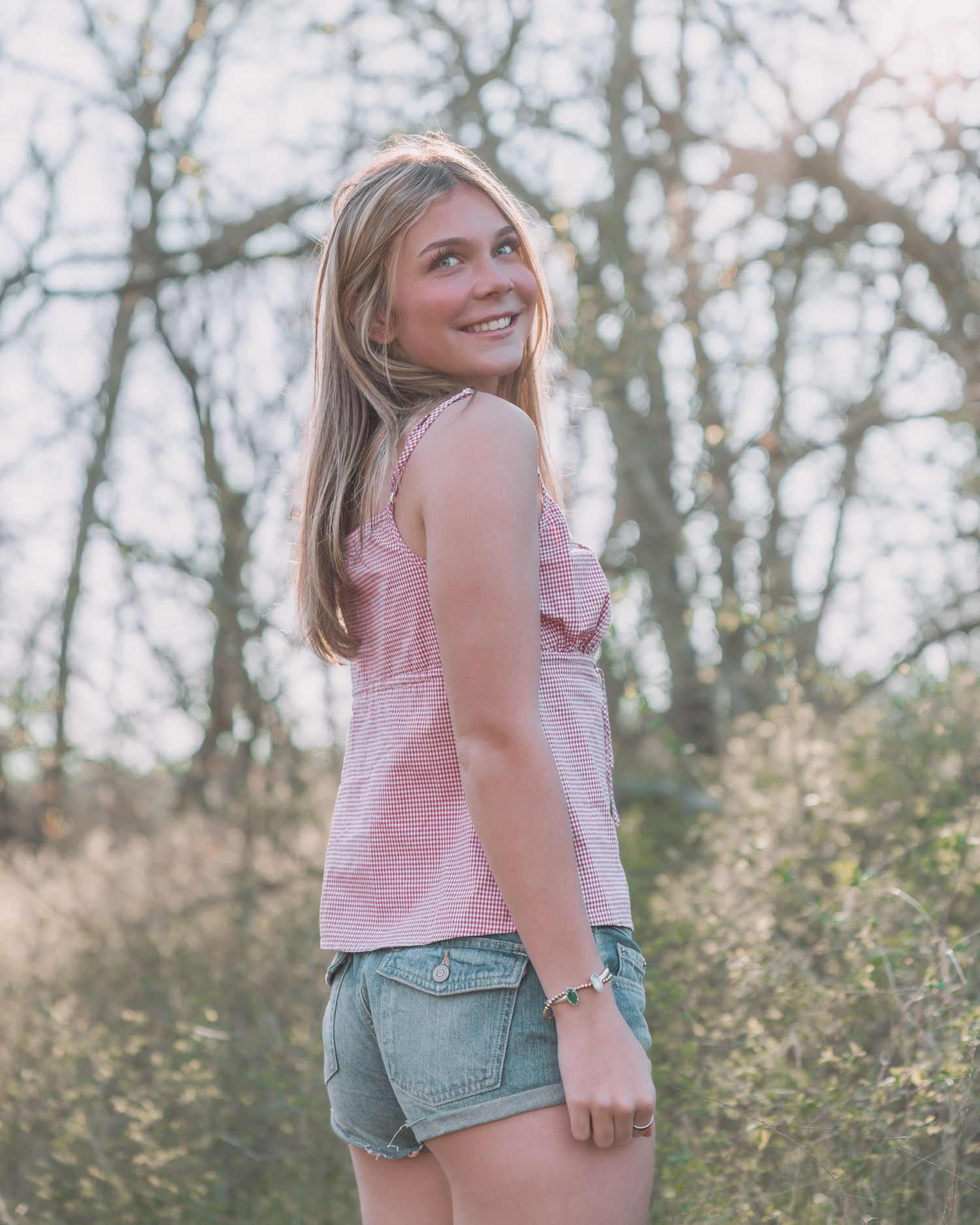 Smiling young blonde woman in pink top and denim shorts standing in nature.